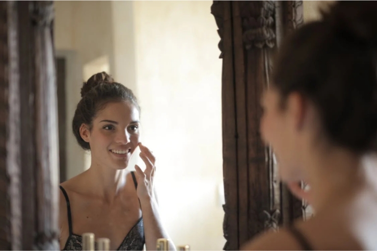 Woman smiling in front of a mirror while applying products to achieve her skincare goals